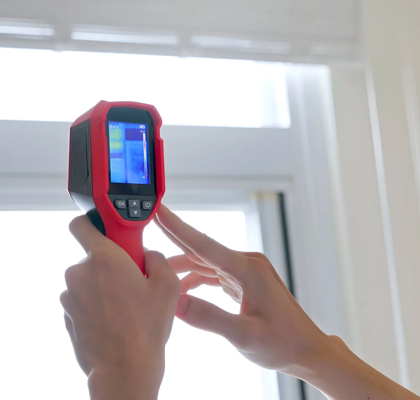 Hands holding a thermal imaging camera up to a bright window to check for heat loss
