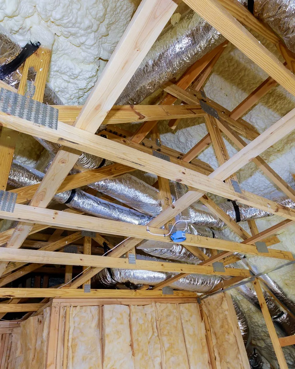 Attic framing with spray foam on the roof deck, foil-wrapped ducts and fiberglass batts between the studs