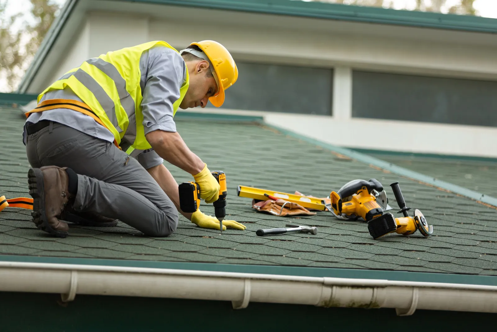 A roofer in a hard hat and safety vest working on a shingle roof