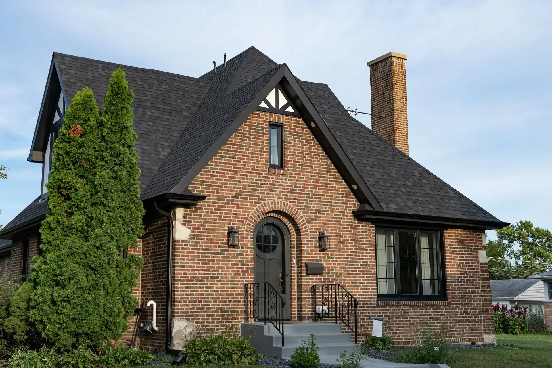 A brick home with a steep dark shingle roof under a clear sky
