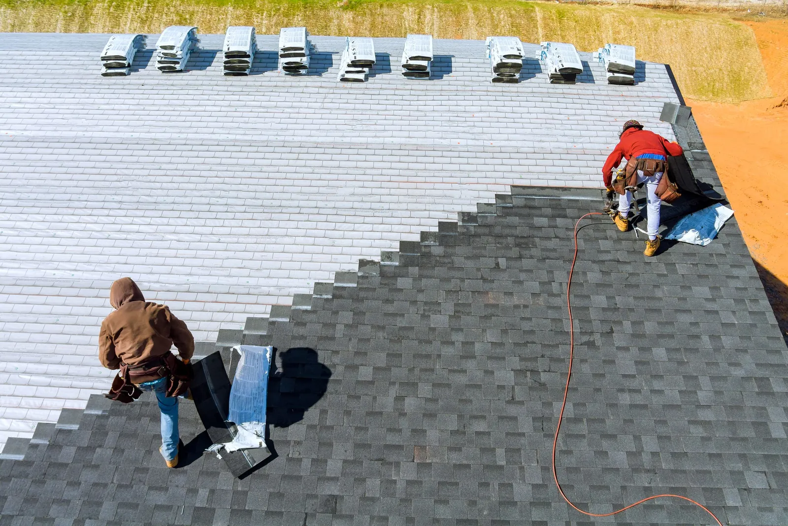 Two roofers nailing new dark shingles over light underlayment, seen from above