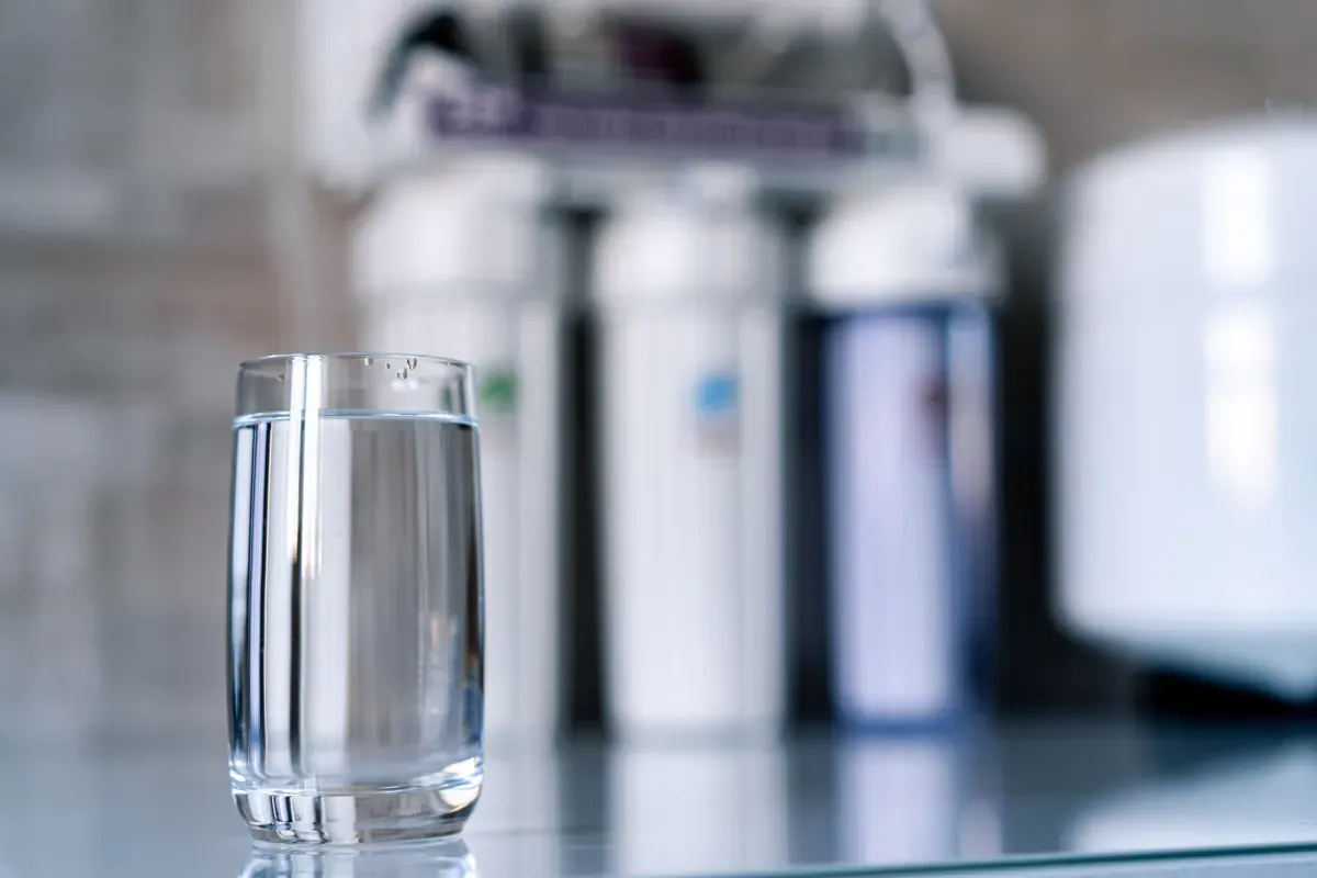 A glass of clear filtered water on a counter in front of a multi-stage filter system