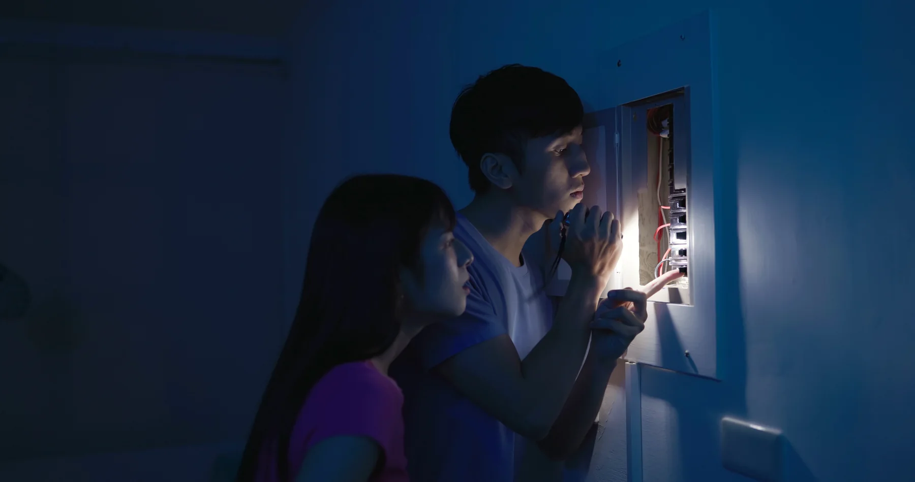 Couple using a flashlight to check the breaker panel during a power outage at night