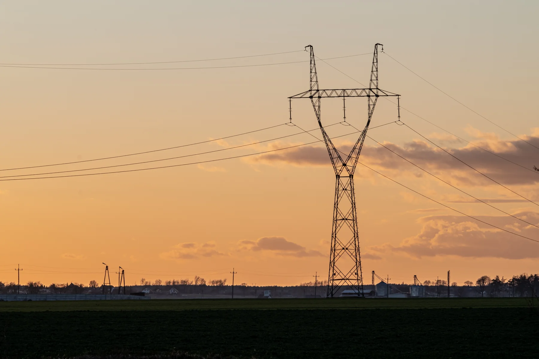 High-voltage transmission tower and power lines silhouetted against an orange sunset sky