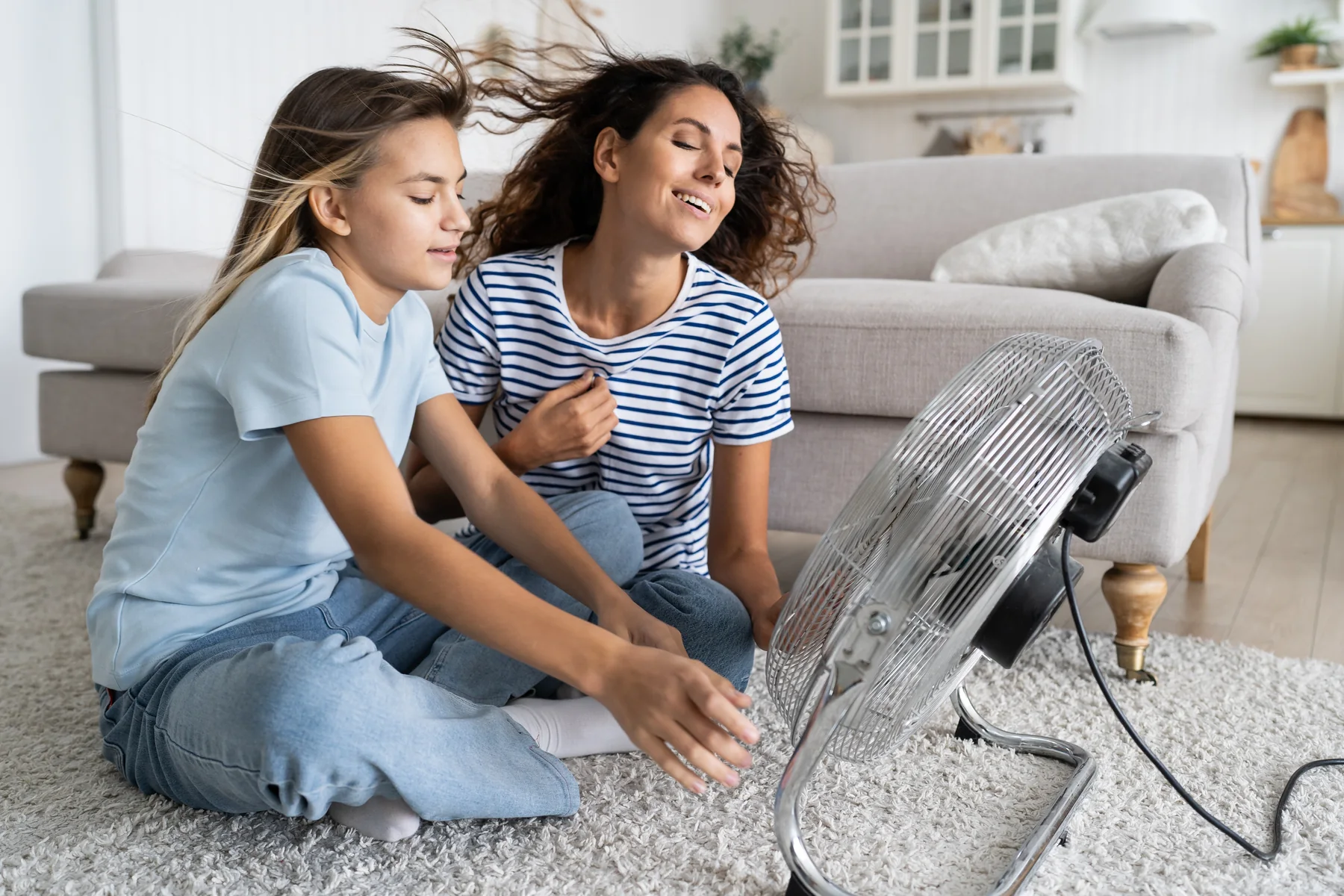 Mother and daughter sitting on a living room rug in front of an electric fan
