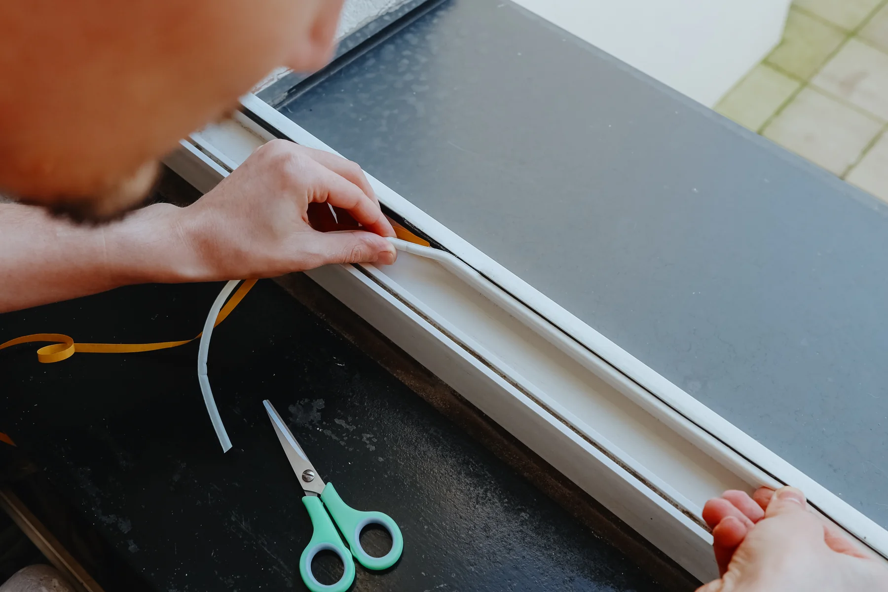 Hands pressing a white weatherstrip seal into the groove of a window frame