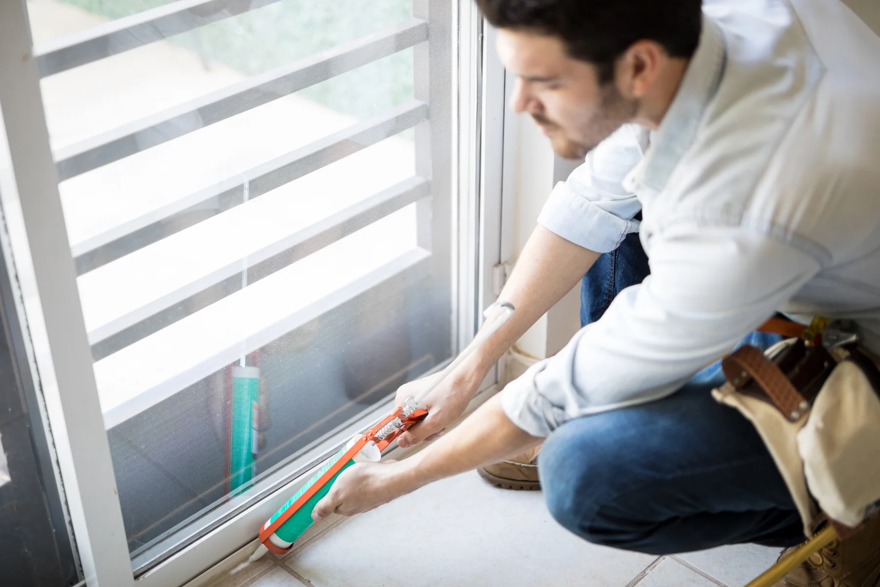 Man kneeling to caulk the bottom edge of a glass door frame
