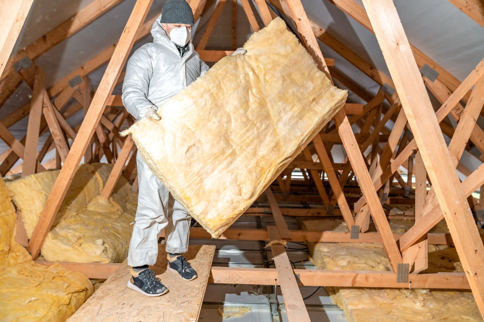 An installer fitting insulation in an attic