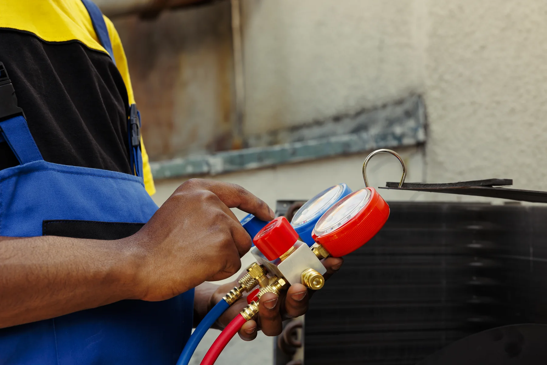 Technician holding a refrigerant manifold gauge set beside an outdoor air conditioning unit