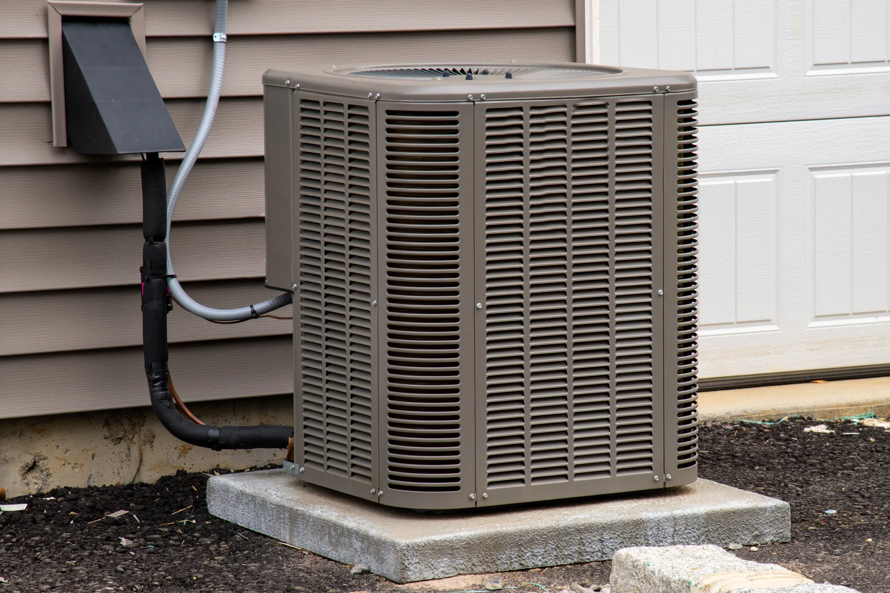 Outdoor air conditioner condenser on a concrete pad next to a house with siding