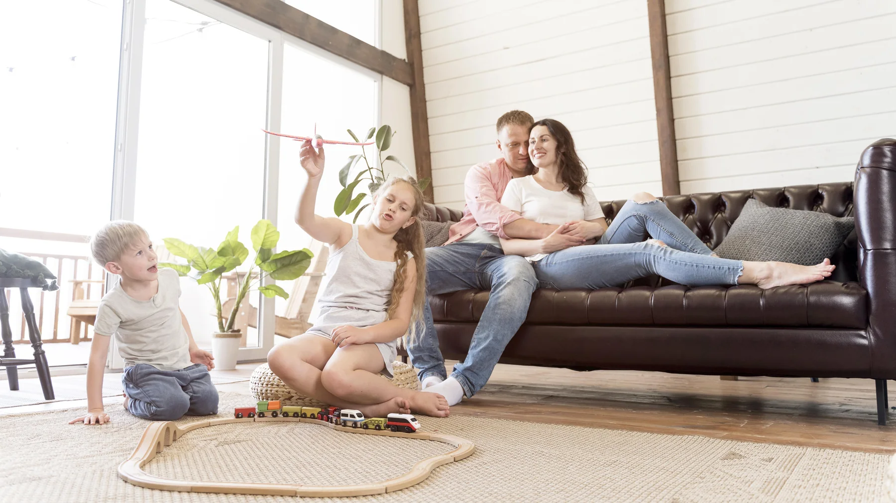 Family relaxing in a bright living room, parents on the sofa and kids playing