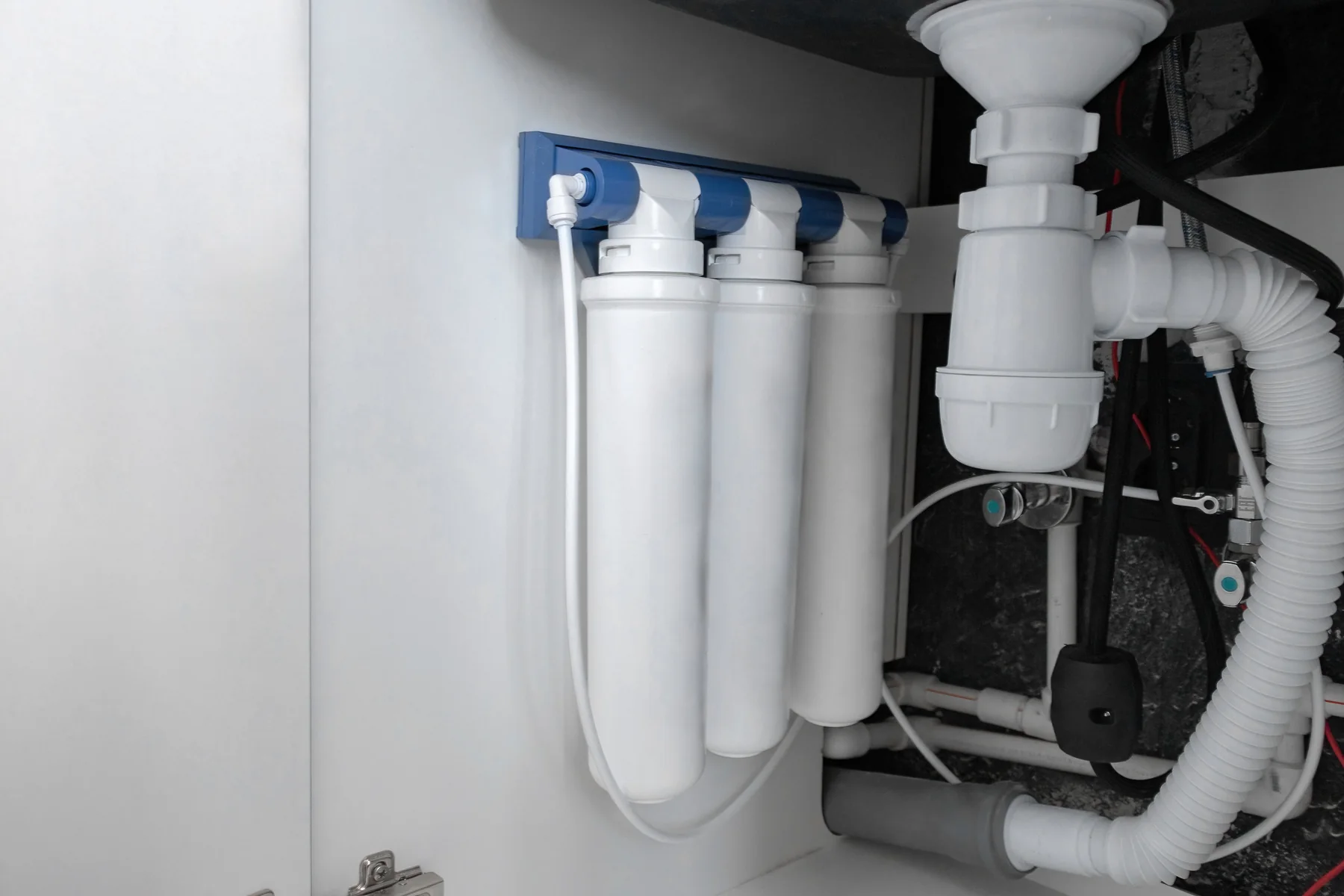 Three-stage under-sink water filtration system with white tubing inside a kitchen cabinet