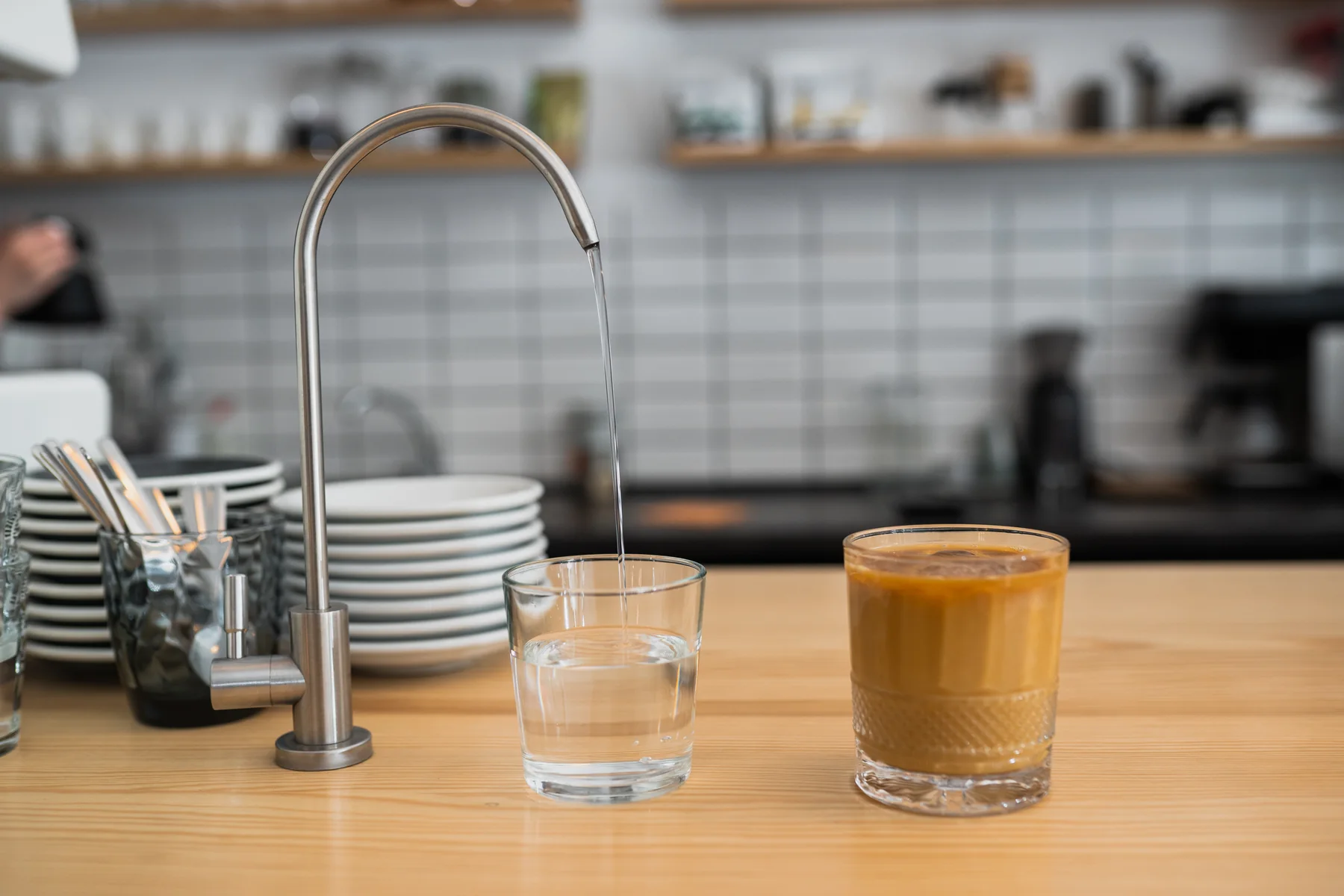 Glass being filled with water from a slim stainless drinking-water faucet on a counter