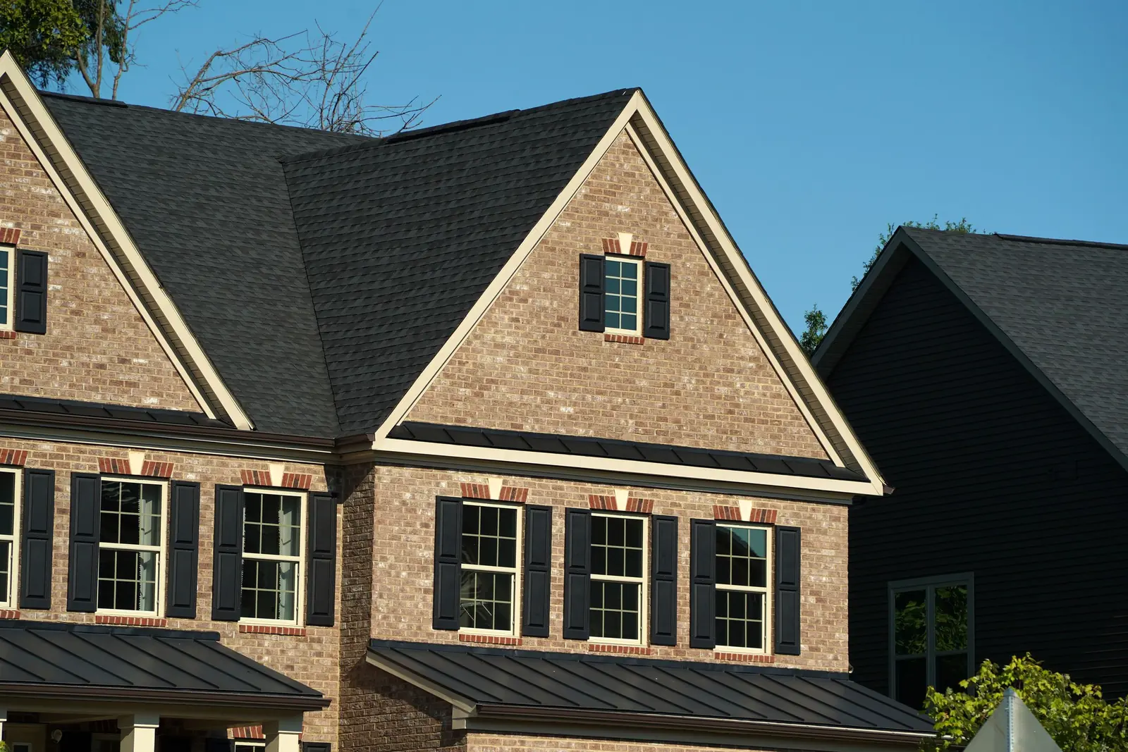 Brick two-storey home with a dark shingle roof under a blue sky